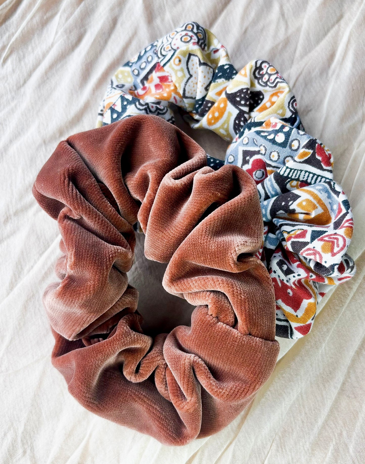 Brown scrunchie and colorful patterned scrunchies on a light fabric background