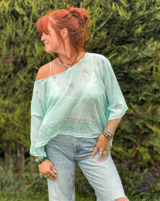 Woman wearing a light green off-shoulder top and ripped jeans standing in a garden.