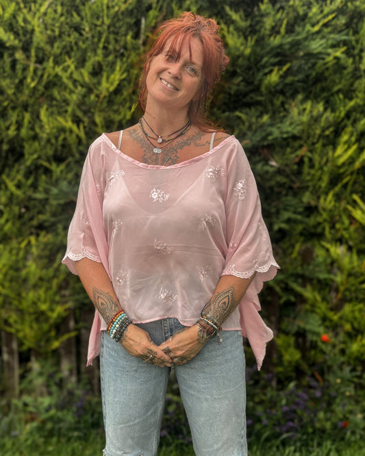 Woman wearing a pink blouse and light blue jeans standing in a garden.