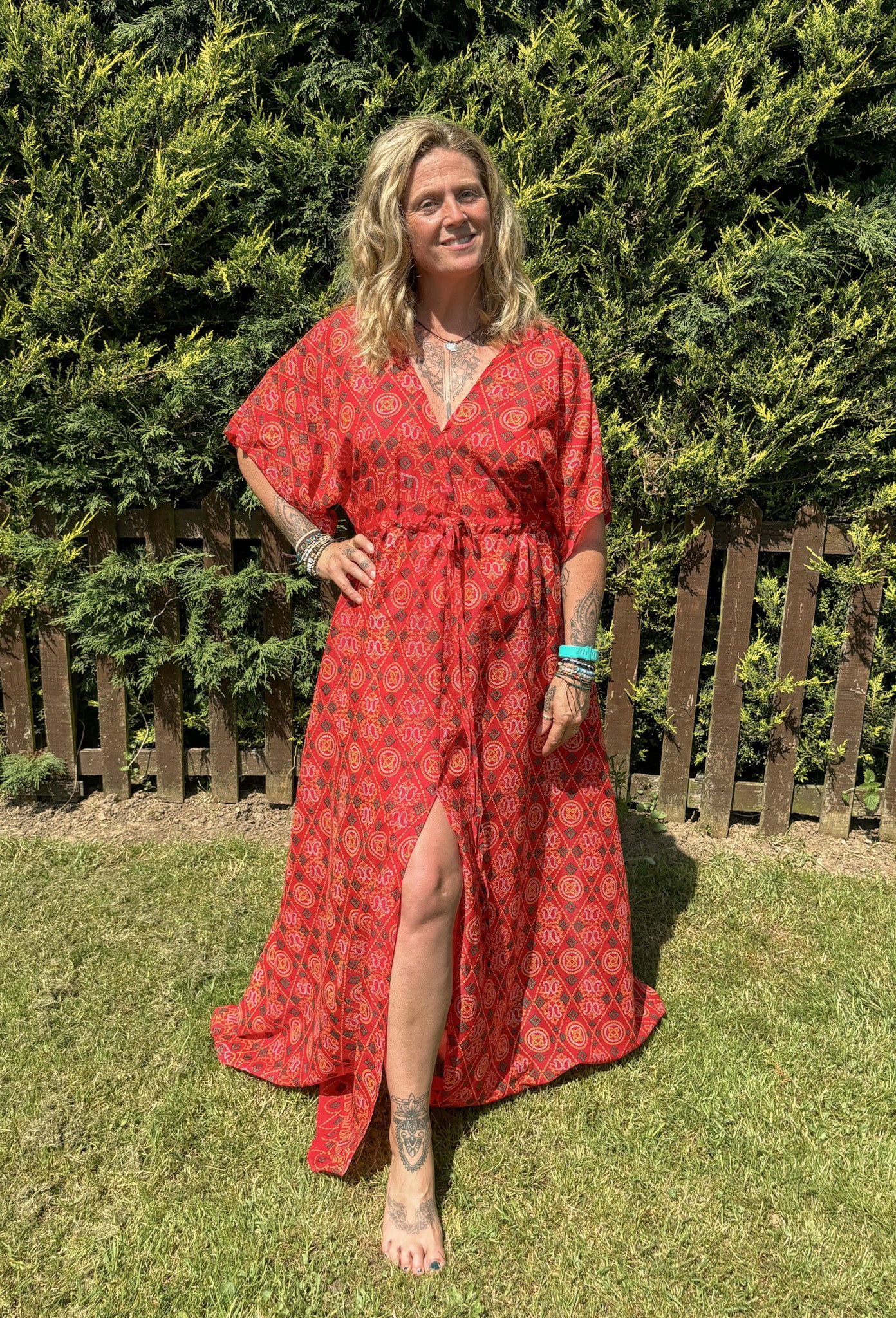Woman in a red patterned dress standing outdoors with greenery in the background