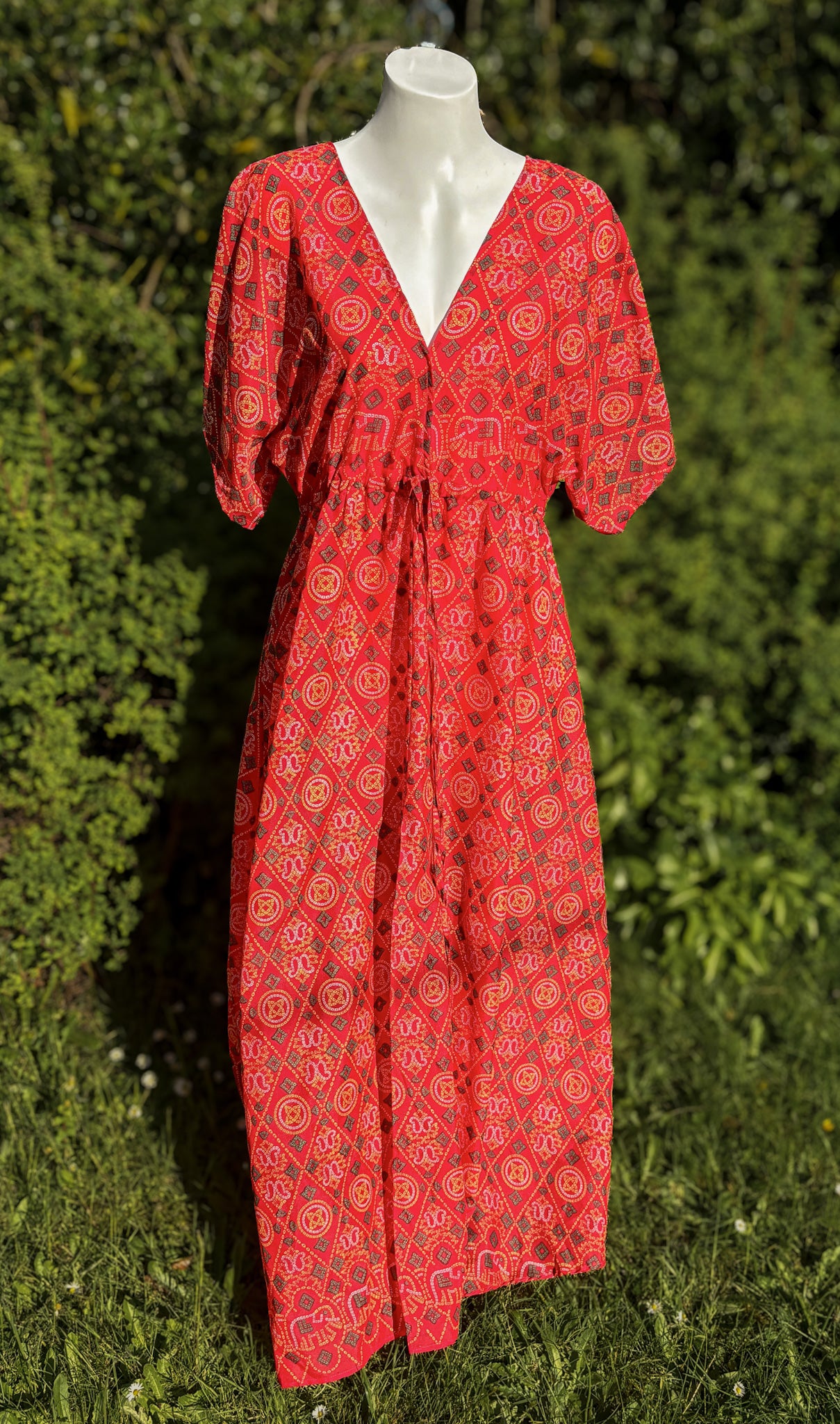 Red patterned dress on a mannequin against a green outdoor background