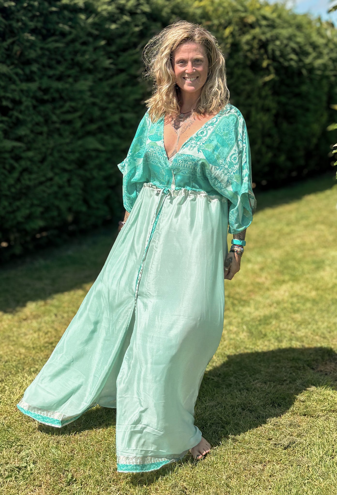 Woman in a teal dress standing on grass with greenery in the background