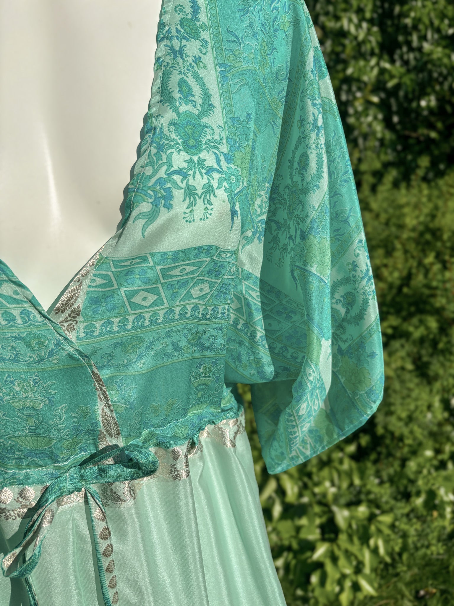 Teal patterned dress on a mannequin with a blurred green outdoor background