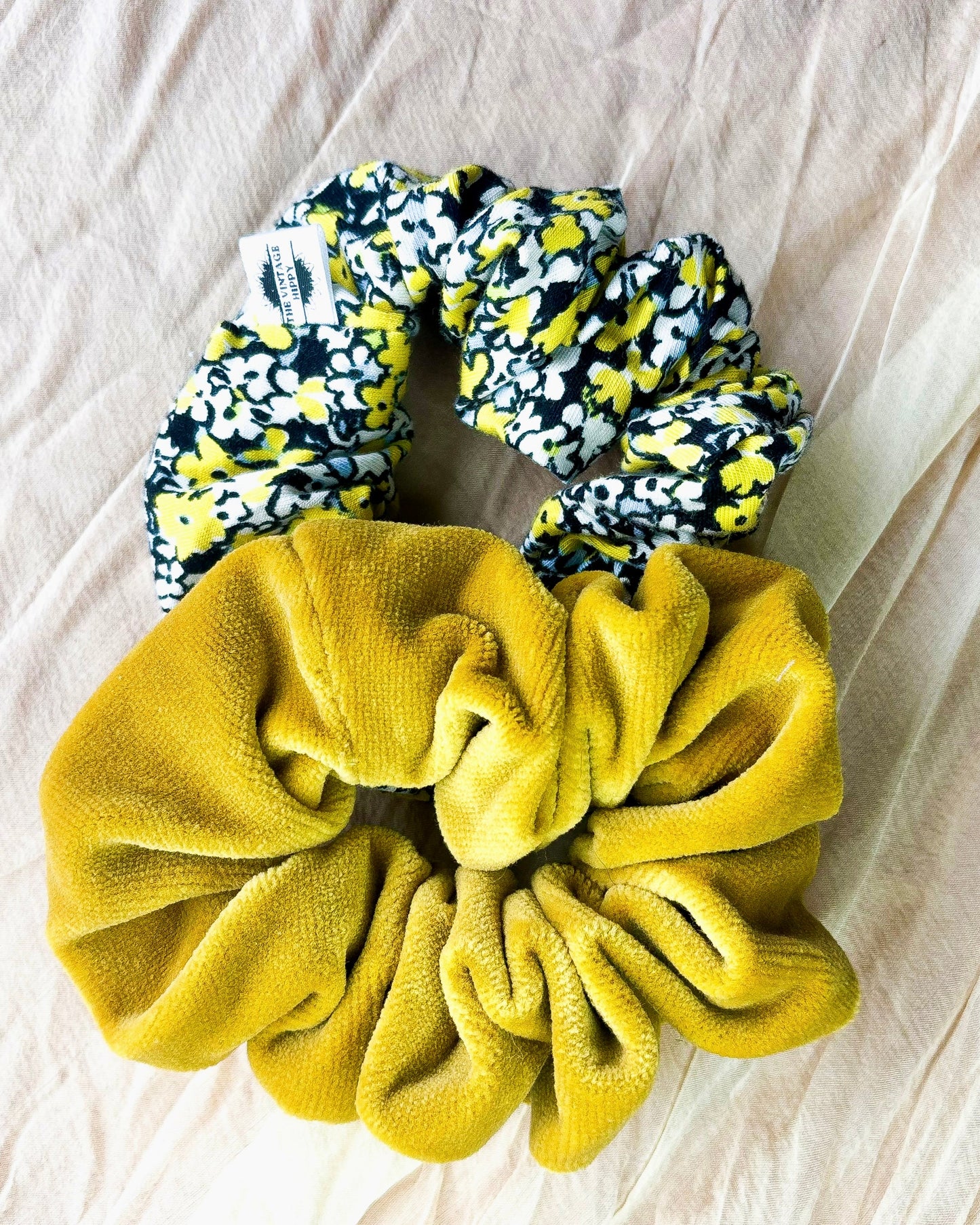 Two scrunchies, one yellow and one floral patterned, on a light fabric background.
