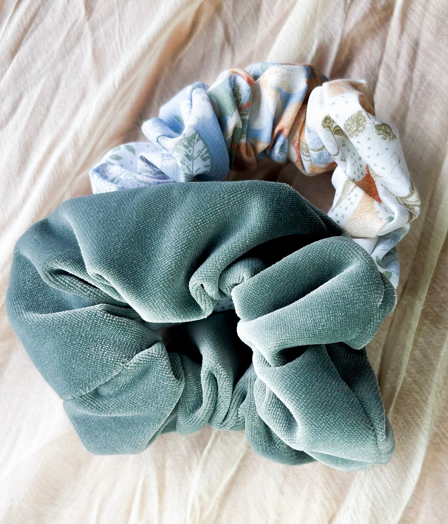 Two scrunchies, one solid color and one patterned, on a light fabric background
