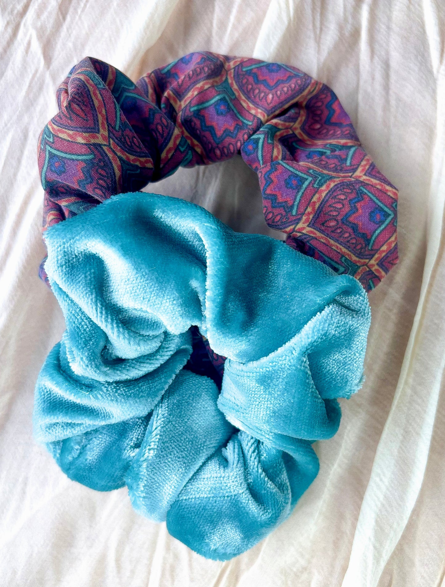 Two scrunchies, one blue and one patterned, on a white fabric background