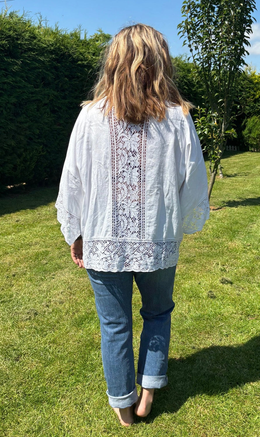 A person standing on grass wearing a white kimono with a floral pattern, paired with blue jeans.