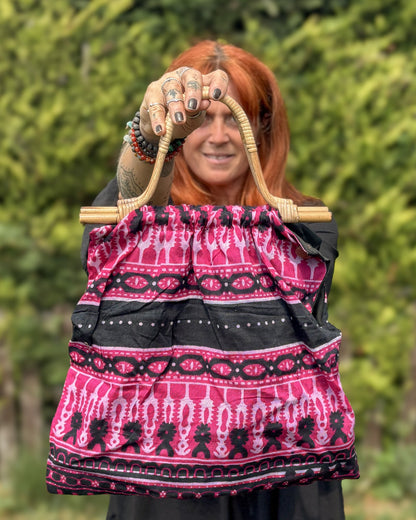 Person holding a pink and black patterned bag with a blurred green background