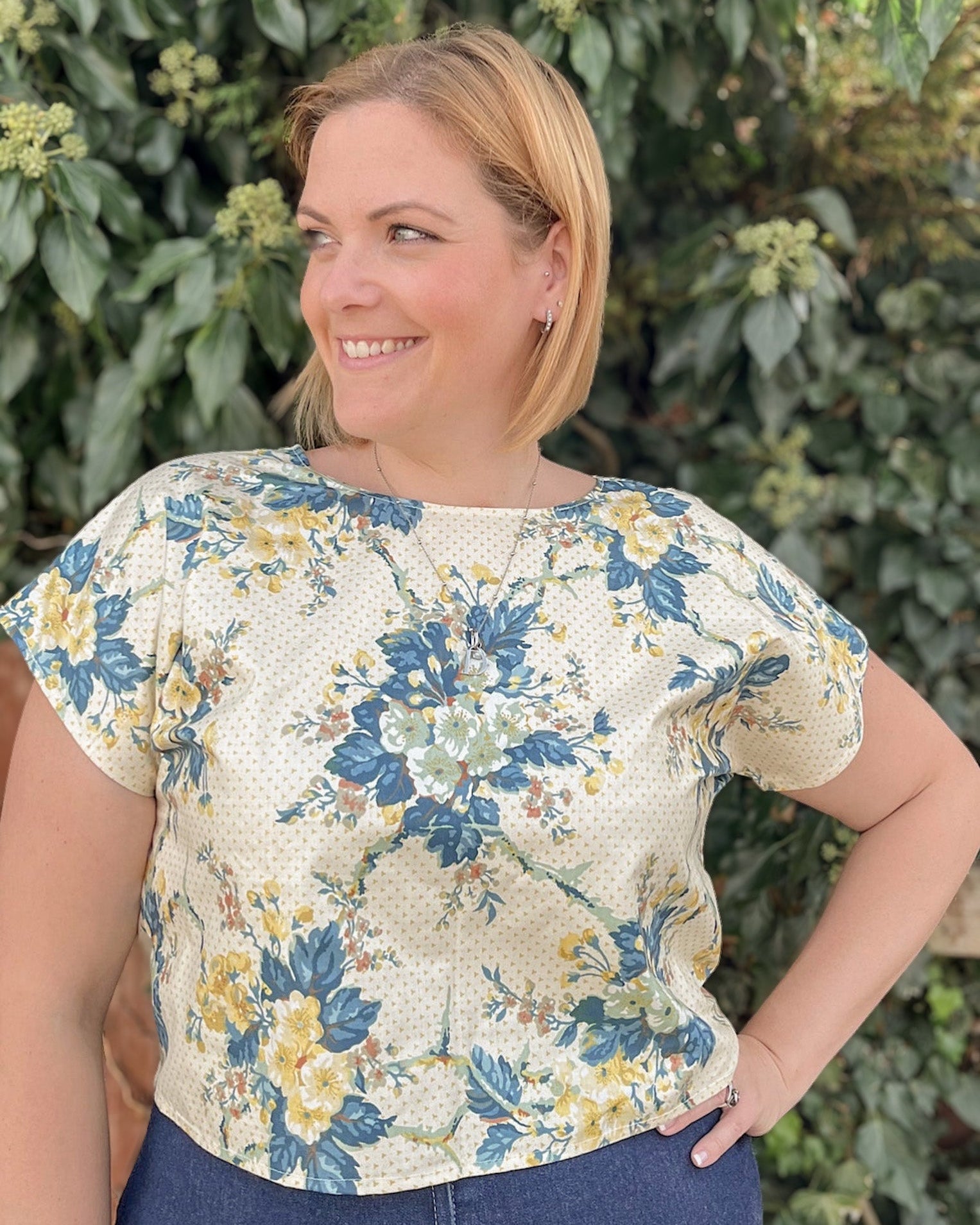 Woman wearing a floral blouse standing in front of green foliage