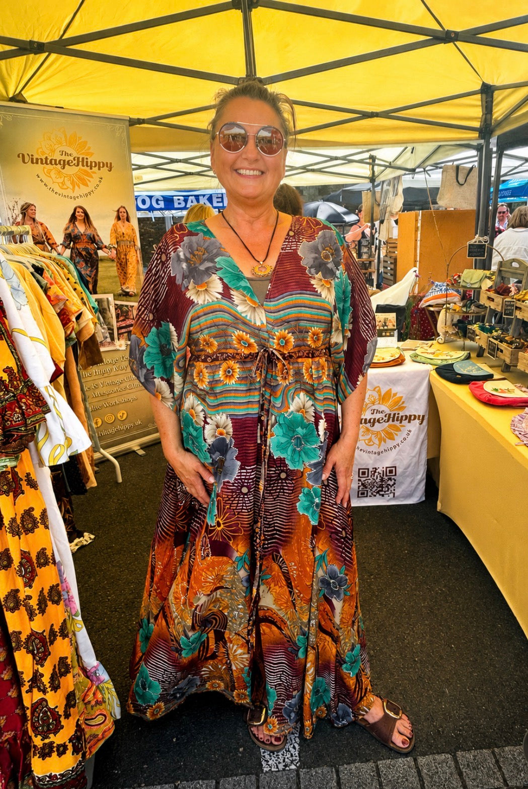 Woman in a colorful dress standing under a yellow tent at an outdoor market.