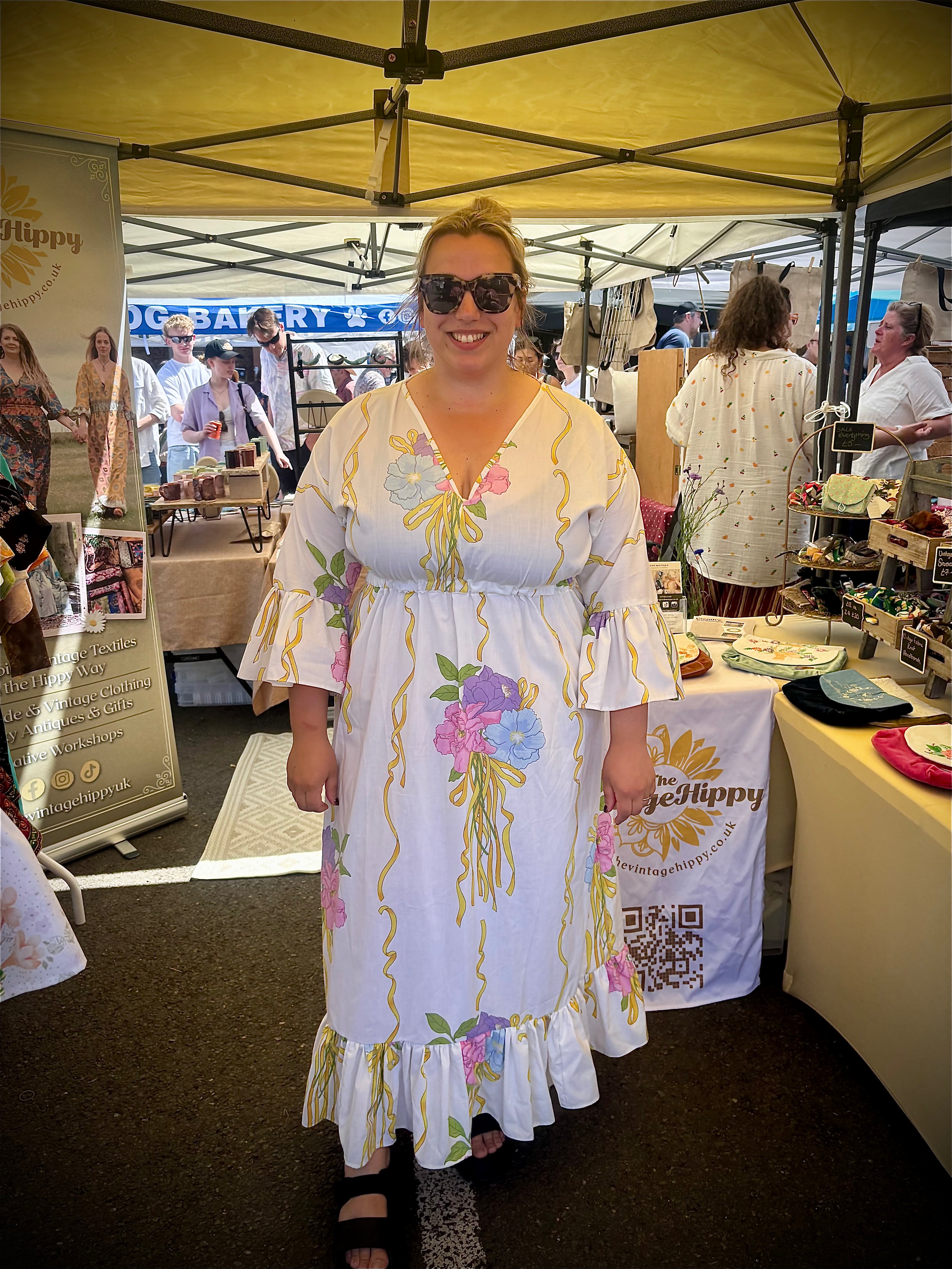 Woman in a floral dress standing under a yellow tent at an outdoor event.