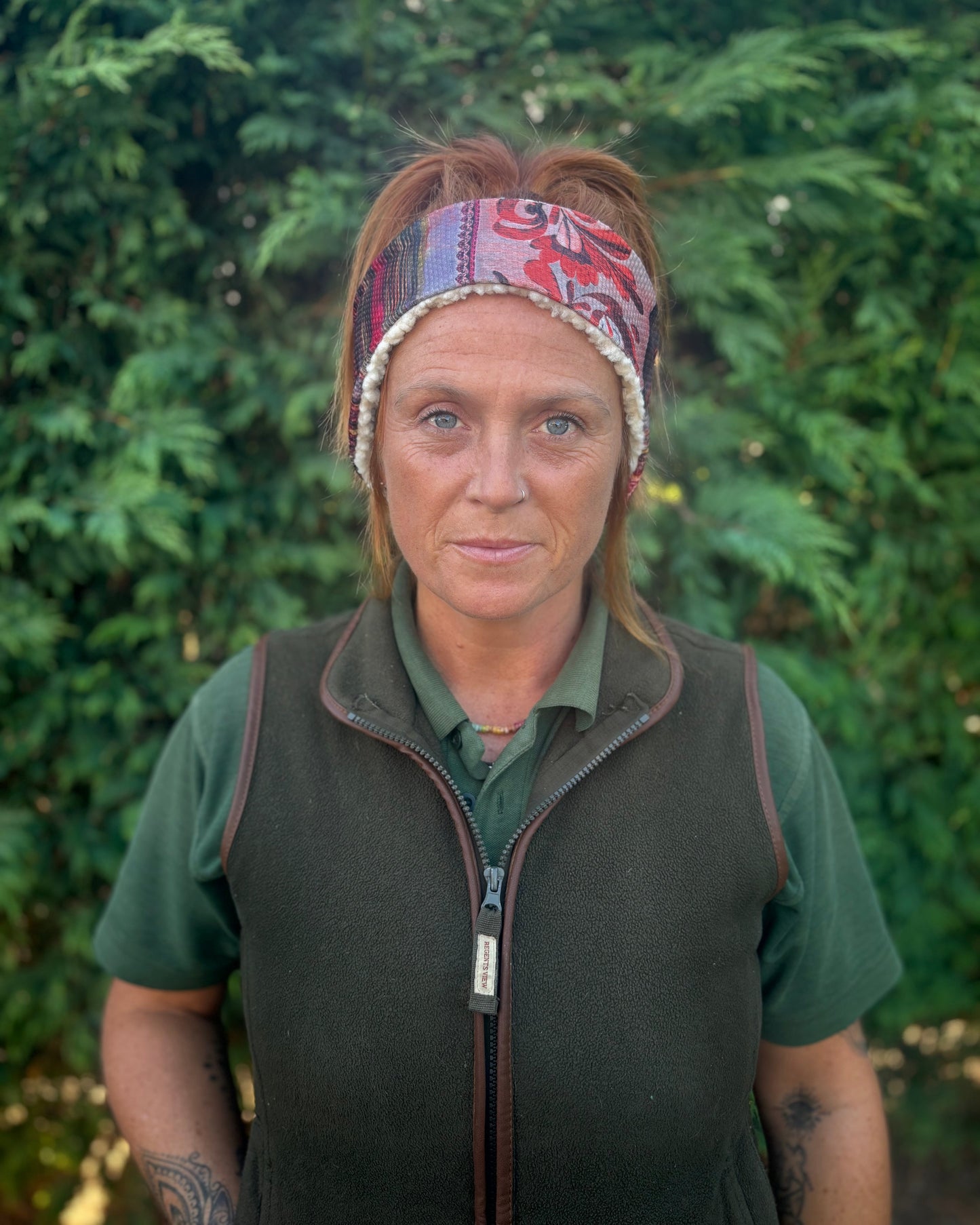 Woman wearing a patterned headband and green shirt with a dark vest against a green background