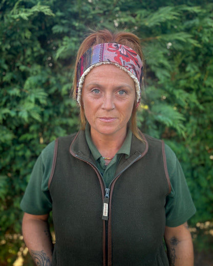 Woman wearing a patterned headband and green shirt with a dark vest against a green background