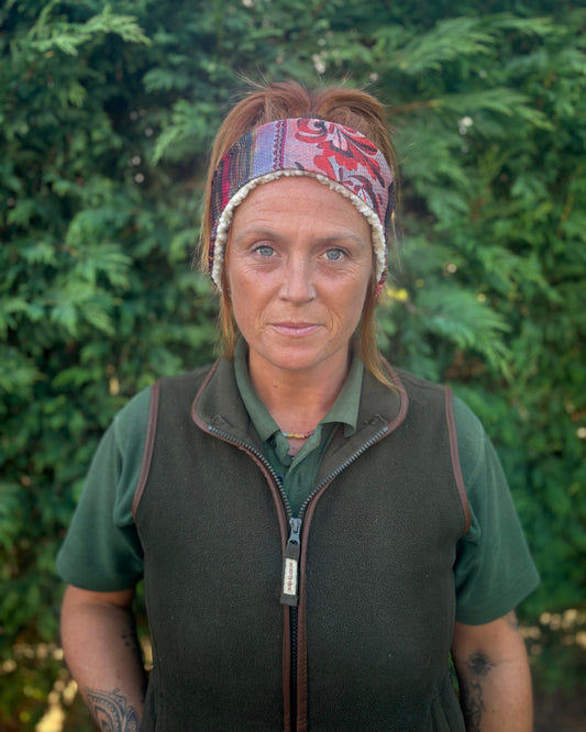 Woman wearing a patterned headband and green shirt with a dark vest against a green background