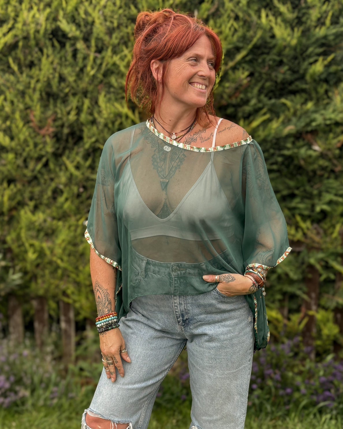 Woman wearing a sheer green top and ripped jeans standing outdoors.
