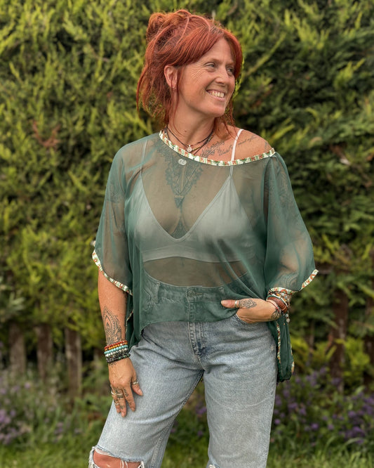 Woman wearing a sheer green top and ripped jeans standing outdoors.