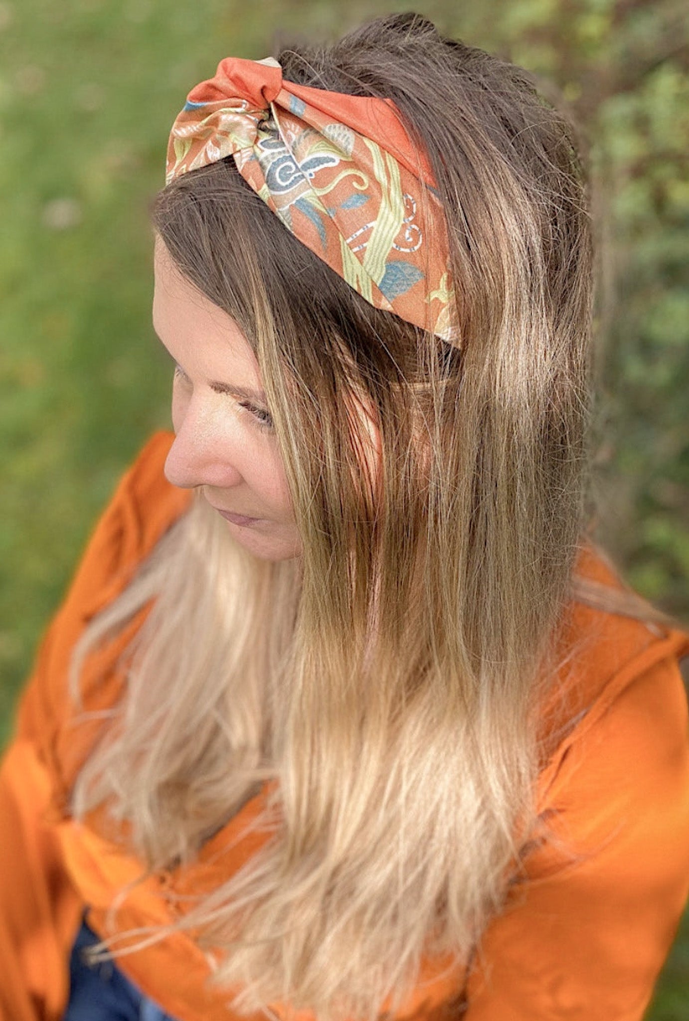 Woman wearing an orange patterned headband with a blurred natural background
