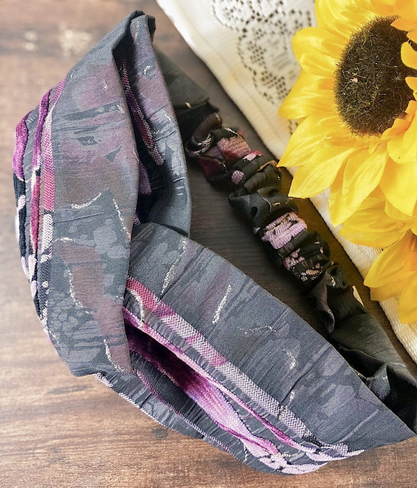 Gray patterned fabric with pink accents on a wooden surface next to a sunflower.