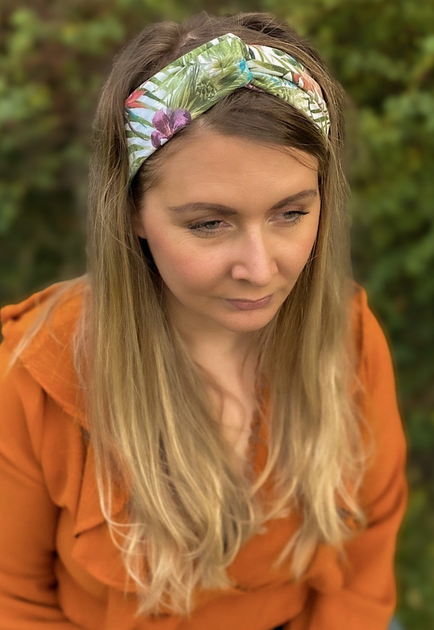 Woman wearing a floral headband with an orange top against a blurred green background