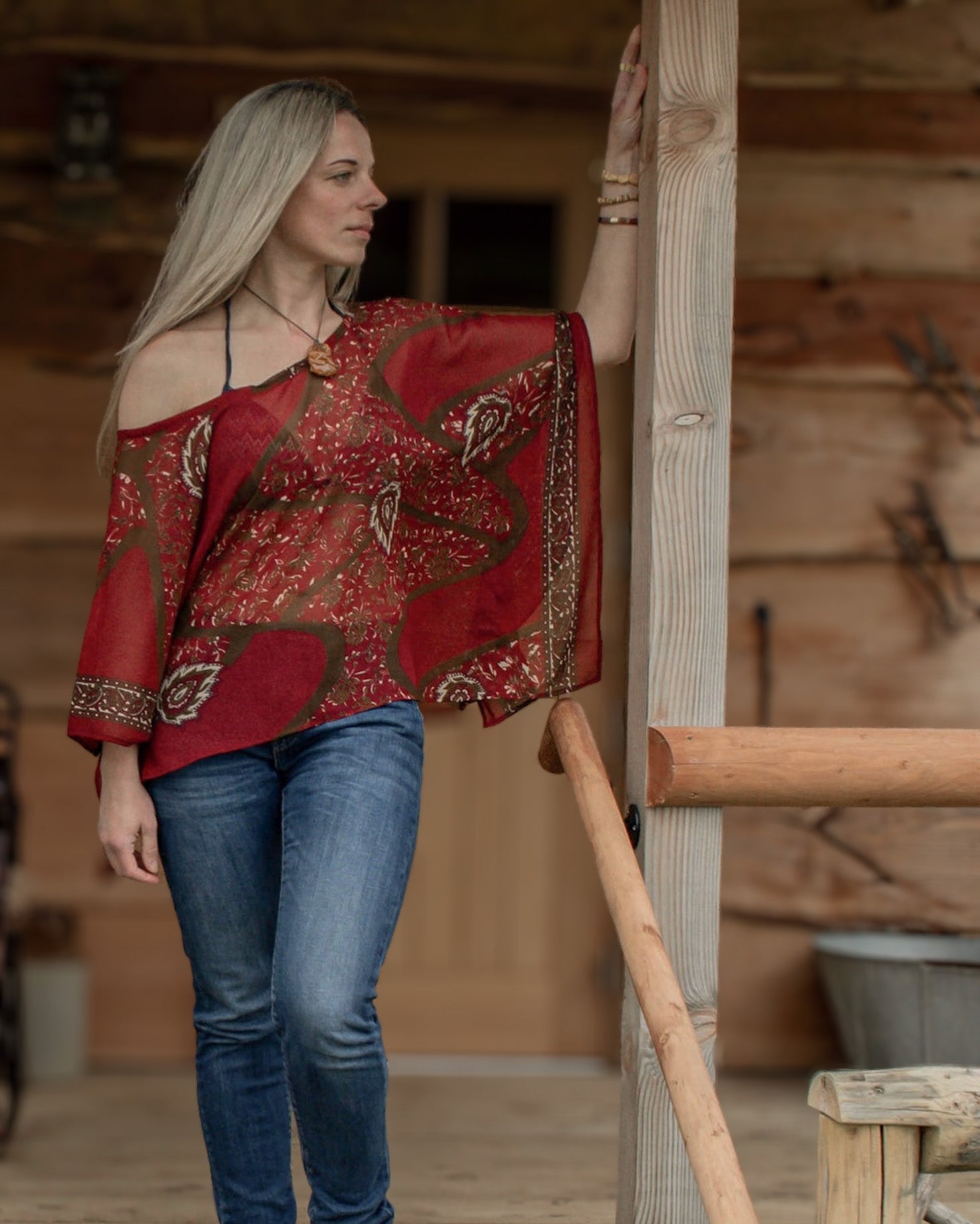 Woman wearing a red patterned top and blue jeans standing in a rustic wooden interior.