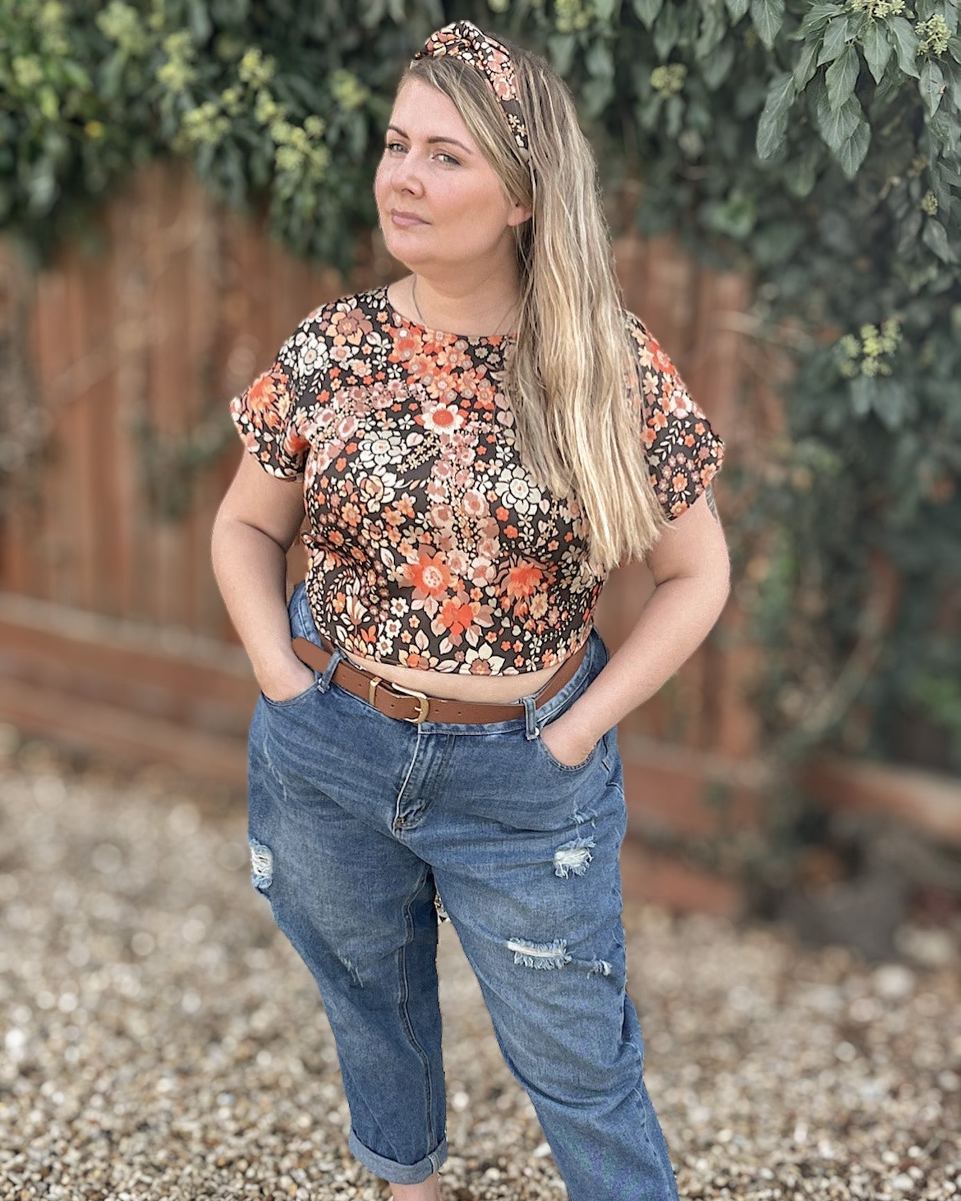 Woman wearing a floral top and jeans standing outdoors with greenery in the background