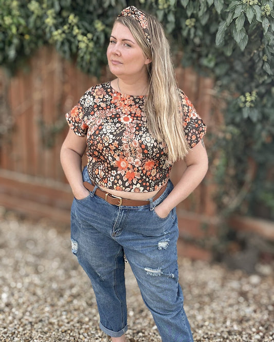 Woman wearing a floral top and jeans standing outdoors with greenery in the background