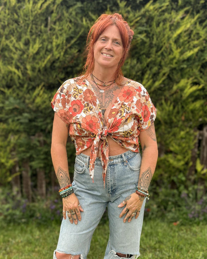 Person wearing a floral top and ripped jeans standing outdoors with greenery in the background