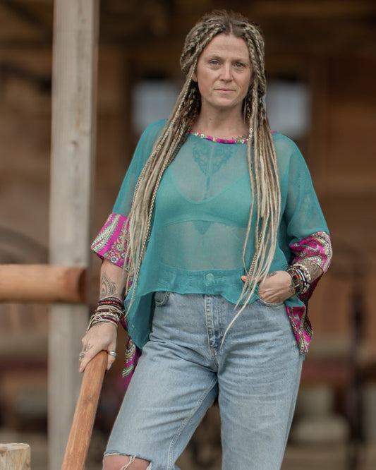 Woman with long braided hair wearing a teal top and ripped jeans, standing outdoors.